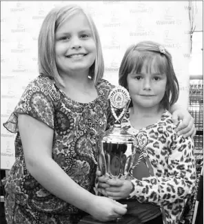  ?? — Photo by Paul Herridge/The Southern Gazette ?? Grace Hart (left), last year’s Janeway Champion Child, symbolical­ly passed the torch, in the form of a trophy, to her successor for 2013-14, Rebekah Winsor, a daughter of Matt and Laura Winsor of Little St. Lawrence, at Walmart in Marystown Wednesday...