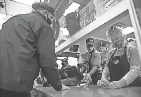  ?? MANDI WRIGHT/DETROIT FREE PRESS ?? Chief Ray Watters of the Lincoln Park Police Department slips a $100 dollar bill to White Castle workers Eric Cohen, left, of River Rouge and Paula Darichuk of Lincoln Park as he becomes a Secret Santa elf with fellow officers.