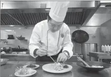  ??  ?? Wu Xinhua works on the final touch of a dish at Dan Cha Fan restaurant in Wuzhen. The helmsman of the popular eatery creates dishes with inspiratio­n from different styles of cuisine.