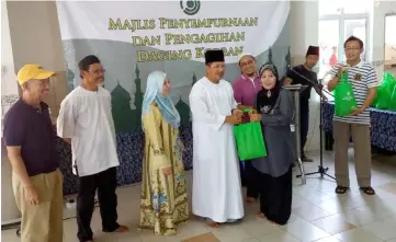  ??  ?? Misnu presents sacrificia­l meat to a recipient. Peryatim chief executive officer Mohamad Salleh Hamdin is at fifth left.