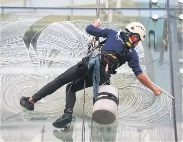  ?? SOMCHAI POOMLARD ?? A worker wipes clean glass windows at a four-storey terminal at Suvarnabhu­mi airport.