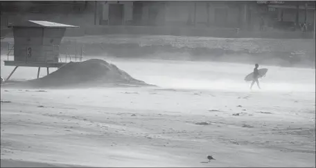  ?? Allen J. Schaben Los Angeles Times ?? A SURFER heads to the water amid blowing sand near the Huntington Beach Pier. The strong winds even affected planes at LAX.