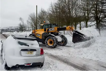  ?? AFP ?? A JCB digger clears snow from the road between Delph and Denshaw in northern England on Friday. —