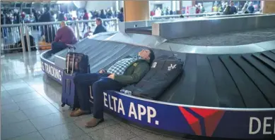  ?? BRANDEN CAMP / ASSOCIATED PRESS LEBANON ?? A traveler sleeps on a baggage carousel at Hartfield-Jackson Atlanta Internatio­nal Airport on Sunday. A sudden power outage at the airport on Sunday grounded hundreds of flights and passengers during one of the busiest travel times of the year.