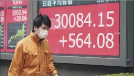  ?? Eugene Hoshiko / Associated­press ?? A man wearing a protective mask walks in front of an electronic stock board showing Japan's Nikkei 225 index Monday in Tokyo.