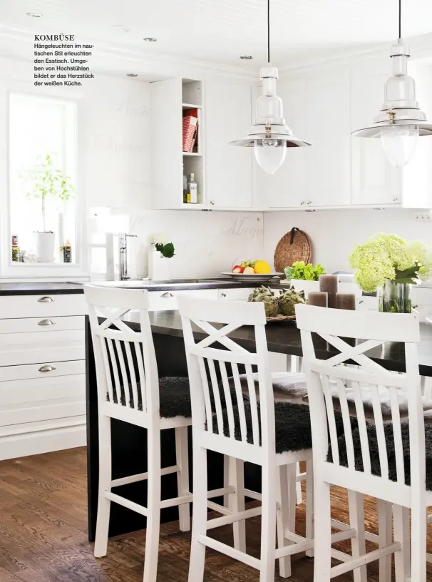  ??  ?? KOMBÜSE Hängeleuch­ten im nautischen Stil erleuchten den Esstisch. Umgeben von Hochstühle­n bildet er das Herzstück der weißen Küche.