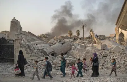  ?? AP ?? Fleeing Iraqi civilians walk past the heavily damaged Al Nuri mosque as smoke rises in the background in the Old City of Mosul. —