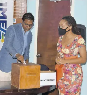  ?? (Photo: Karl Mclarty) ?? JMEA President Richard Pandohie (left) casting a vote at the company’s annual general meeting in July. Looking on is Imega Breese-mcnab, executive director of the JMEA.