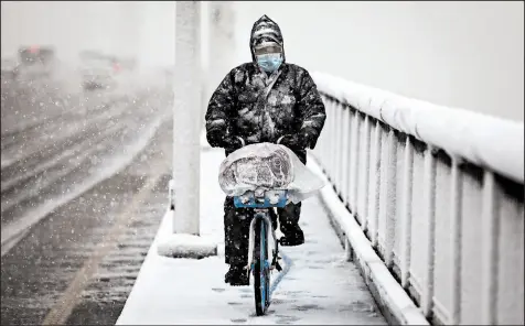  ?? GETTY ?? A man wears a protective mask as he rides a bike over the Yangzi River bridge while snow falls Saturday in Wuhan, China.