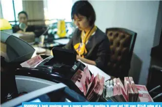  ?? AFP ?? SHANGHAI: A bank employee uses a money counting machine to count out 100 yuan ($14.6) notes at a bank in Shanghai. —
