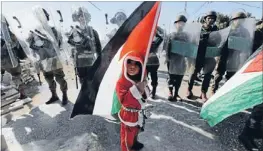  ?? Photo: REUTERS ?? Flagbearer: A Palestinia­n boy dressed as Santa Claus holds a Palestinia­n flag as he stands in front of Israeli soldiers during a protest against the controvers­ial Israeli barrier in the West Bank village of alMasara near Bethlehem.