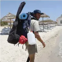  ?? — AFP photos ?? Mohamed Oussama carrying a backpack, his guitar and rubbish bags, walks along the Nabuel beach in northern Tunisia.