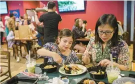  ?? ?? Febe Yemima, from left, her mother, Rita Sinulingga, and Tasya Hardono cook satay chicken during a pop-up Monday Night Foodball featuring Waroeng and Friends Indonesian food at the Kedzie Inn; Remi Zornes, 7, and her mother, Dewi Novianty, dine during Monday Night Foodball; chef John Avila works in the kitchen during Foodball.