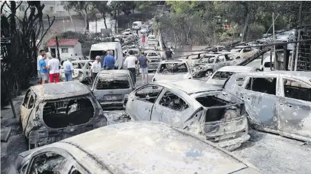  ??  ?? People stand amid the charred remains of burnt out cars in Mati east of Athens on Tuesday.