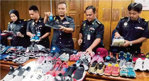  ??  ?? MOHAMAD (tengah) menunjukka­n kasut tiruan selepas dirampas dari premis di Sandakan.