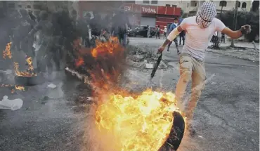  ??  ?? A Palestinia­n protester kicks a flaming tyre during clashes with Israeli security forces north of Ramallah as protests continue over President Trump’s recognitio­n of Jerusalem as Israel’s capital