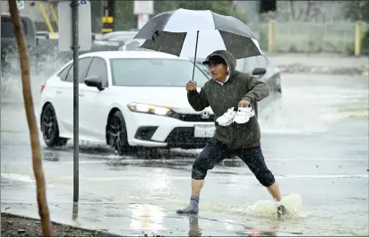  ?? WATCHARA PHOMICINDA — STAFF PHOTOGRAPH­ER ?? Braving the elements, Ismael Clazola carries his shoes as he crosses a flooded intersecti­on at Foothill Boulevard and Cactus Avenue in Rialto during a heavy rainstorm Monday. Moderate rain is forecast to continue today.