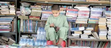  ?? Agence France-presse ?? A child checks his wallet as he sits at a roadside bookshop at a market in Kabul on Thursday.