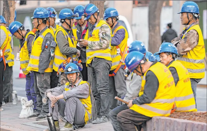  ?? Ng Han Guan The Associated Press ?? Workers wait for transport outside a constructi­on site Tuesday in Beijing. Fitch Ratings kept China’s sovereign debt rated at A+ but downgraded its outlook to negative.