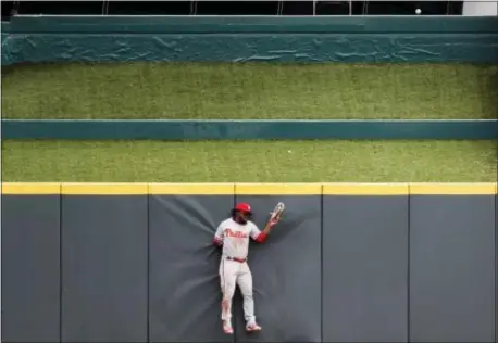  ?? JOHN MINCHILLO — THE ASSOCIATED PRESS ?? Phillies center fielder Odubel Herrera crashes into the outfield wall as a solo home run hit by the Reds’ Michael Lorenzen bounces off the grass embankment in the bottom of the sixth inning Thursday in Cincinnati. The Reds won 7-4.