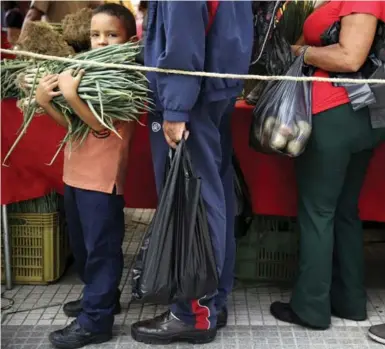  ?? NACHO DOCE/REUTERS ?? People have to line up for whatever they can get in Venezuela — in this case an armload of chives at a street market.