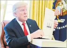  ?? Mike Theiler / Bloomberg ?? U.S. President Donald Trump holds up a tax-overhaul bill after signing it into law in the Oval Office of the White House in Washington on Friday.