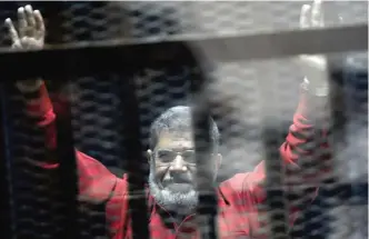  ?? — AP ?? CAIRO: In this file photo, former Egyptian President Mohammed Morsi, wearing a red jumpsuit that designates he has been sentenced to death, raises his hands inside a defendants cage in a makeshift courtroom at the national police academy, in an eastern...