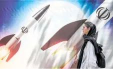  ?? Bearing the — AFP file photo ?? A woman walks past a banner depicting launching missiles emblem of the Islamic Republic of Iran in central Tehran.