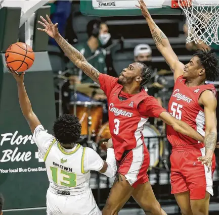  ?? Mike Carlson / Associated Press ?? South Florida's Justin Brown has his shot defended by UH’s DeJon Jarreau (3) and Brison Gresham in the first half. Jarreau had 17 points on 8-of-13 shooting along with eight assists and four rebounds as the Cougars pulled away from the Bulls in the second half.