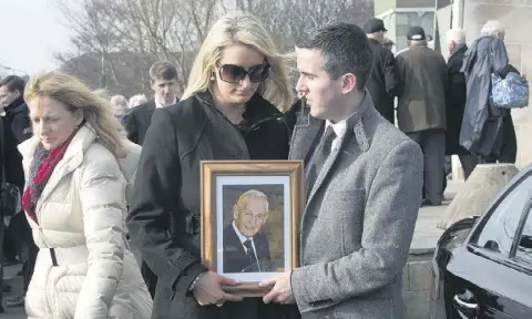  ??  ?? LEGACY: Aisling Connolly, granddaugh­ter of Sean Og O Ceallachai­n, and her husband Barry Connolly hold a photo of the legendary sports broadcaste­r at his funeral Mass at Our Lady Mother of Divine Grace Church, Raheny, Dublin last week