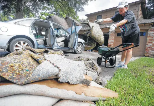  ?? Melissa Phillip / Houston Chronicle ?? Susan Henney tosses wet carpet Wednesday as she helps her neighbors clean up from flooding in the Lakewood Forest subdivisio­n.