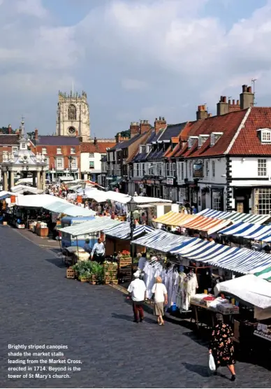  ??  ?? Brightly striped canopies shade the market stalls leading from the Market Cross, erected in 1714. Beyond is the tower of St Mary’s church.