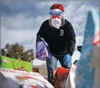  ??  ?? Dressed as a COVID-19safe Santa, Jose Gonzalez helps sort dozens of Christmas presents Sunday (Dec. 20) in the Enos Garcia Elementary School parking lot. Jose and his partner, Vannesa Gonzalez, organized a toy drive for Taos’ undocument­ed immigrant community through their advocacy group, Sin Fronteras Nuevo México. During the drive-by gift collection event, the pair handed out 170 presents to about 90 families.