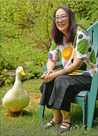  ?? SEAN D. ELLIOT/THE DAY ?? Author Debbi Michiko Florence sits in the garden outside her Norwich office with Darcy, her 6-year-old Peking duck pet.