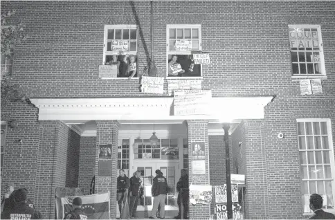  ?? — AFP photo ?? Pro-Maduro activists, occupying the Venezuelan Embassy, hold signs from the windows and display posters on the facade as federal agents open the door in Washington DC.