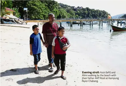  ??  ?? Evening stroll: Azizi (left) and Alimi walking by the beach with their father Aliff Rosli at Kampung Nyior Chabang.