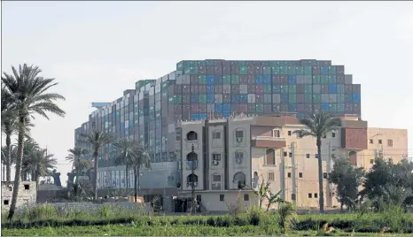  ?? AHMAD HASSAN / AFP ?? The container ship Ever Given towers over a four-story building along the Suez Canal in Egypt. The ship has been wedged across the canal for most of the past week, stoppering one of the world’s busiest shipping routes.