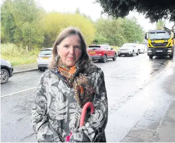  ??  ?? Traffic concerns Irene Campbell on Petersburn Road. A number of parked cars are visible behind her, while a lorry passes the new £17m Hilltop Primary School campus