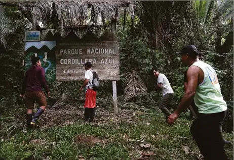  ?? Martin Mejia / Associated Press ?? A group of men pass in front of a sign for the Cordillera Azul National Park in the Peru Amazon, on Oct. 3. Residents in Kichwa Indigenous villages in Peru say they fell into poverty after the government turned their ancestral forest into a national park, restricted hunting and sold forest carbon credits to oil companies.