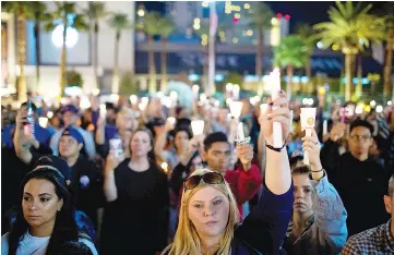  ?? — AFP photo ?? Mourners attend a candleligh­t vigil at the corner of Sahara Avenue and Las Vegas Boulevard for the victims of Sunday night’s mass shooting.