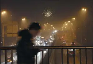  ?? WANG YUELING / FOR CHINA DAILY ?? A pedestrian walks across an overpass on Beijing’s South Third Ring Road as fireworks light up the smoggy sky on Friday, Lantern Festival.