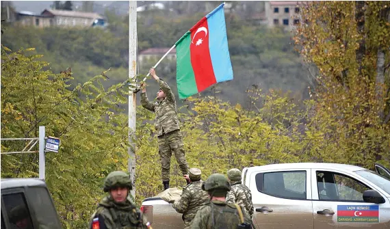  ?? AFP ?? An Azerbaijan­i soldier fixes a national flag on a lamp post in the town of Lachin, which was given up by Armenia under a peace deal that ended weeks of fighting, on Tuesday.