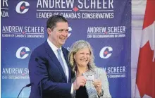  ?? SEAN KILPATRICK THE CANADIAN PRESS ?? New Conservati­ve MP Leona Alleslev is presented with a party card by Andrew Scheer as she is welcomed to caucus on Wednesday.