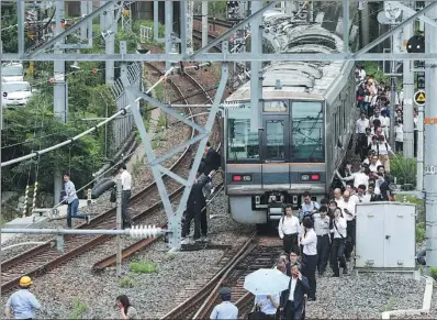  ?? JIJI PRESS / AFP ?? Passengers from a train walk along railroad tracks after rail service was suspended following an earthquake in Osaka on Monday. Most of the railway and bullet train services resumed later in the day.