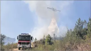  ?? AP PHOTO ?? A firefighti­ng plane drops its load near a fire engine battling a wild fire in the village of Pucarica, near Abrantes, central Portugal, Aug.11.