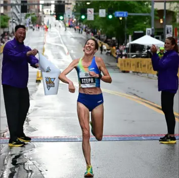  ?? Lucy Schaly/Post-Gazette ?? Former Steelers quarterbac­k Charlie Batch lets go of the tape at left as Stephanie Bruce pumps her fist at the finish line after she finished first in the women’s half marathon on the Blvd. of the Allies Downtown on Sunday.