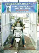  ?? ALFIAN RIZAL/JAWA POS ?? MATERIAL BEKAS: Pengendara sepeda motor memasuki bilik sprayer yang dipasang di gerbang Perumahan SPR, Keputih, kemarin.