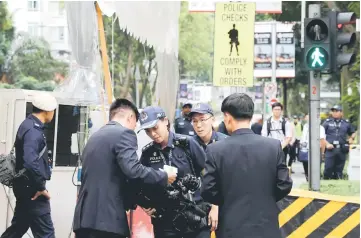  ??  ?? Police inspect a North Korean cameraman outside St Regis hotel before he enters the regulated zone, in Singapore.