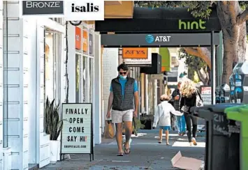  ?? JUSTIN SULLIVAN/GETTY ?? A pedestrian walks by a retail store that has reopened in San Francisco.