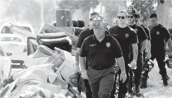  ??  ?? Firefighte­rs walk around debris removed from homes during a door-to-door survey of a flooded neighbourh­ood in Houston on Thursday.